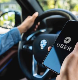 BERLIN, GERMANY JULY 2019: Uber driver holding smartphone in car. Uber is an American company offering transportation services online. Illustrative editorial.