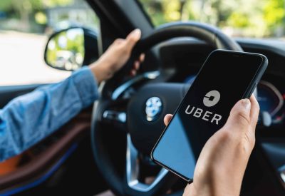 BERLIN, GERMANY JULY 2019: Uber driver holding smartphone in car. Uber is an American company offering transportation services online. Illustrative editorial.